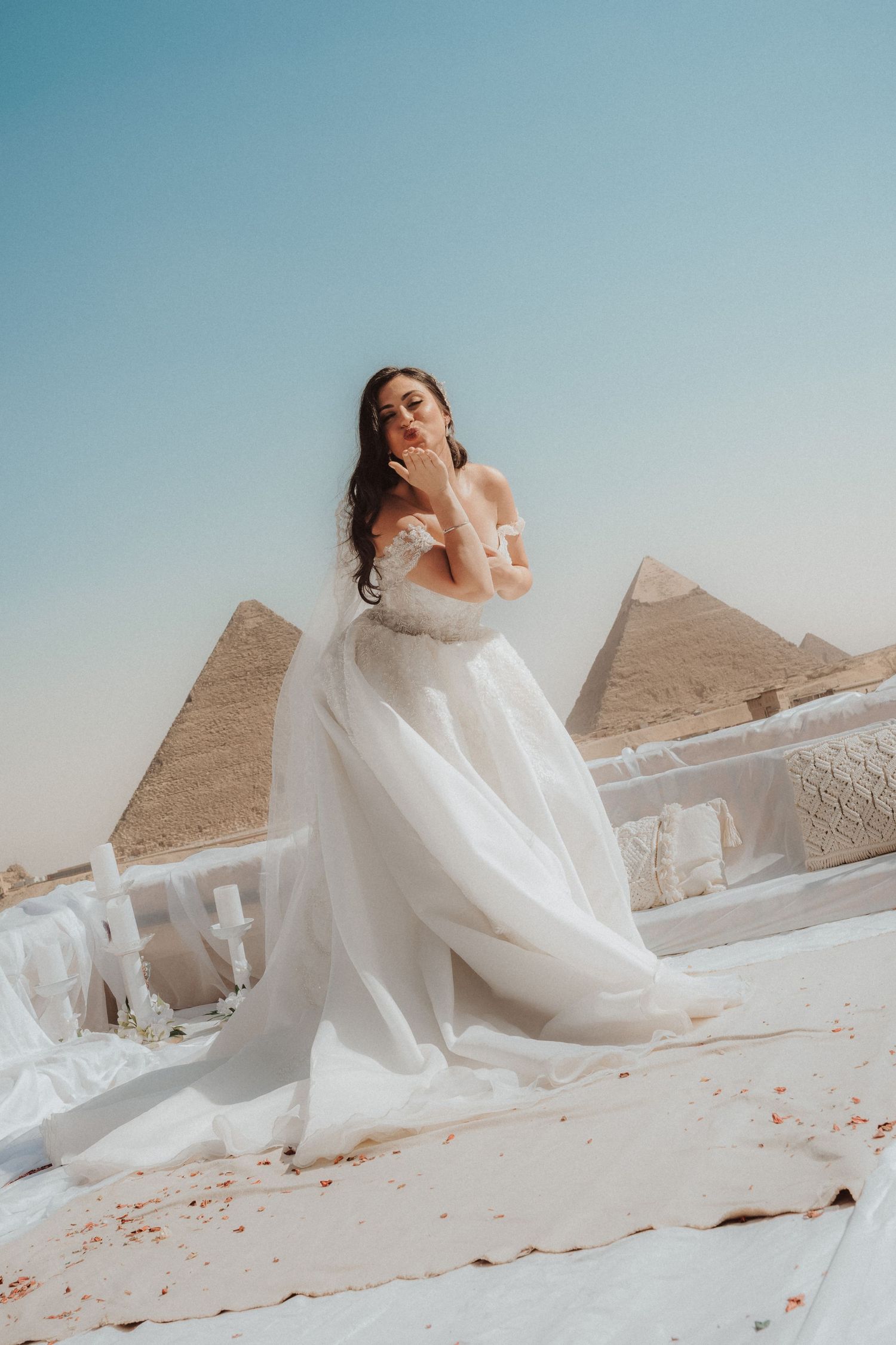 A person in a flowing white wedding dress poses gracefully against the backdrop of the ancient Egyptian pyramids at Giza.