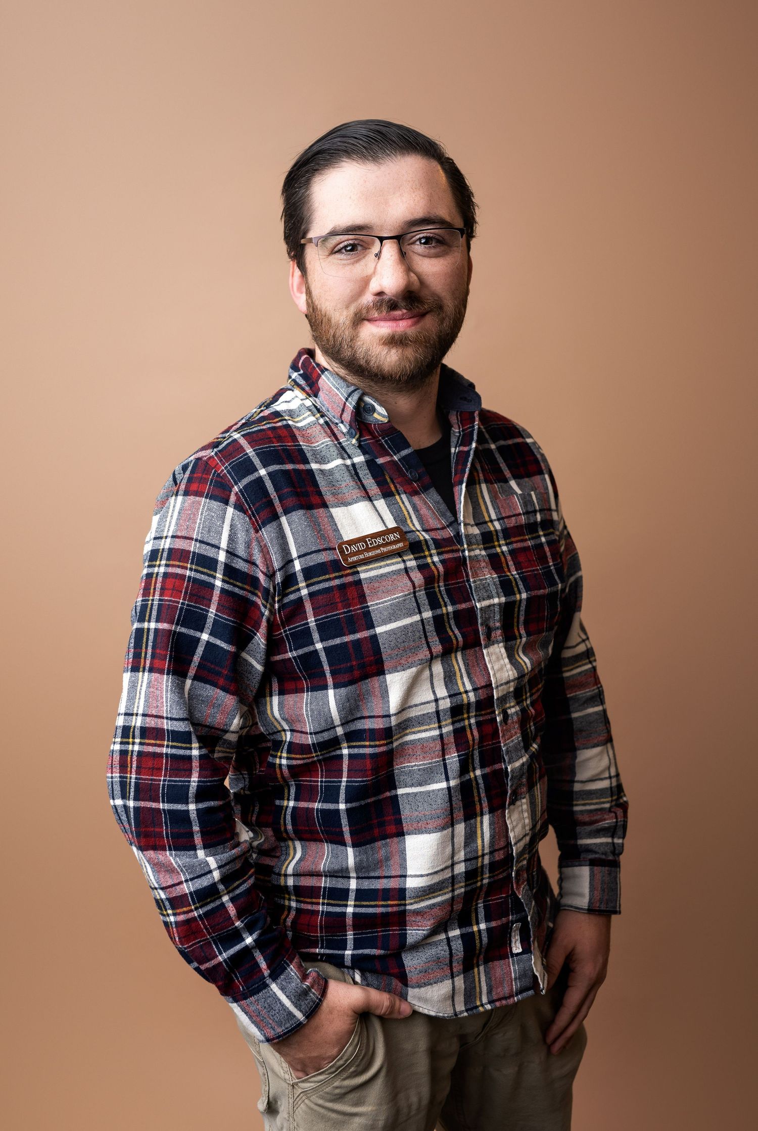 A person wearing a plaid flannel shirt and khaki pants poses against a brown backdrop in a photo series.