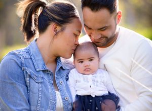 Young mother and father sitting together and kissing their baby's head - Kelly Chapman Photographer Perth