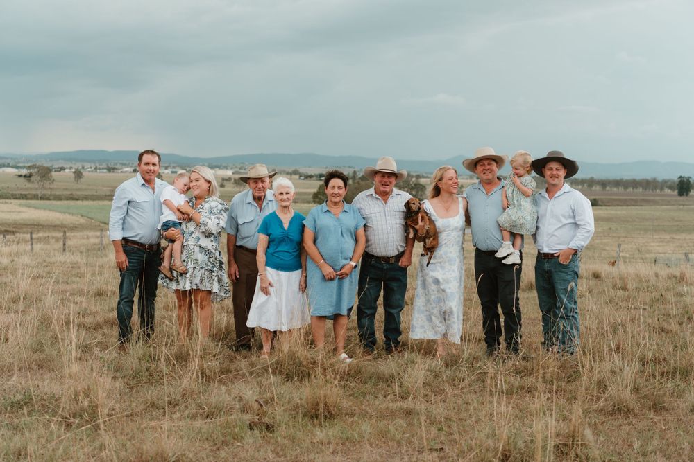 A group of ten people in casual Western attire posing together in a rural field under a cloudy sky.