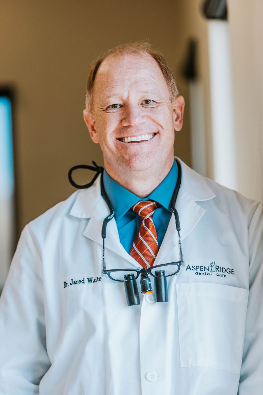 Healthcare professional wearing white coat and loupes in medical office setting.