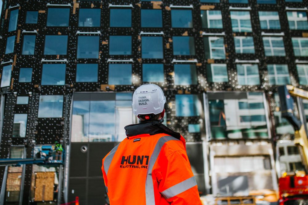 Construction worker in orange safety vest inspecting modern glass building facade.