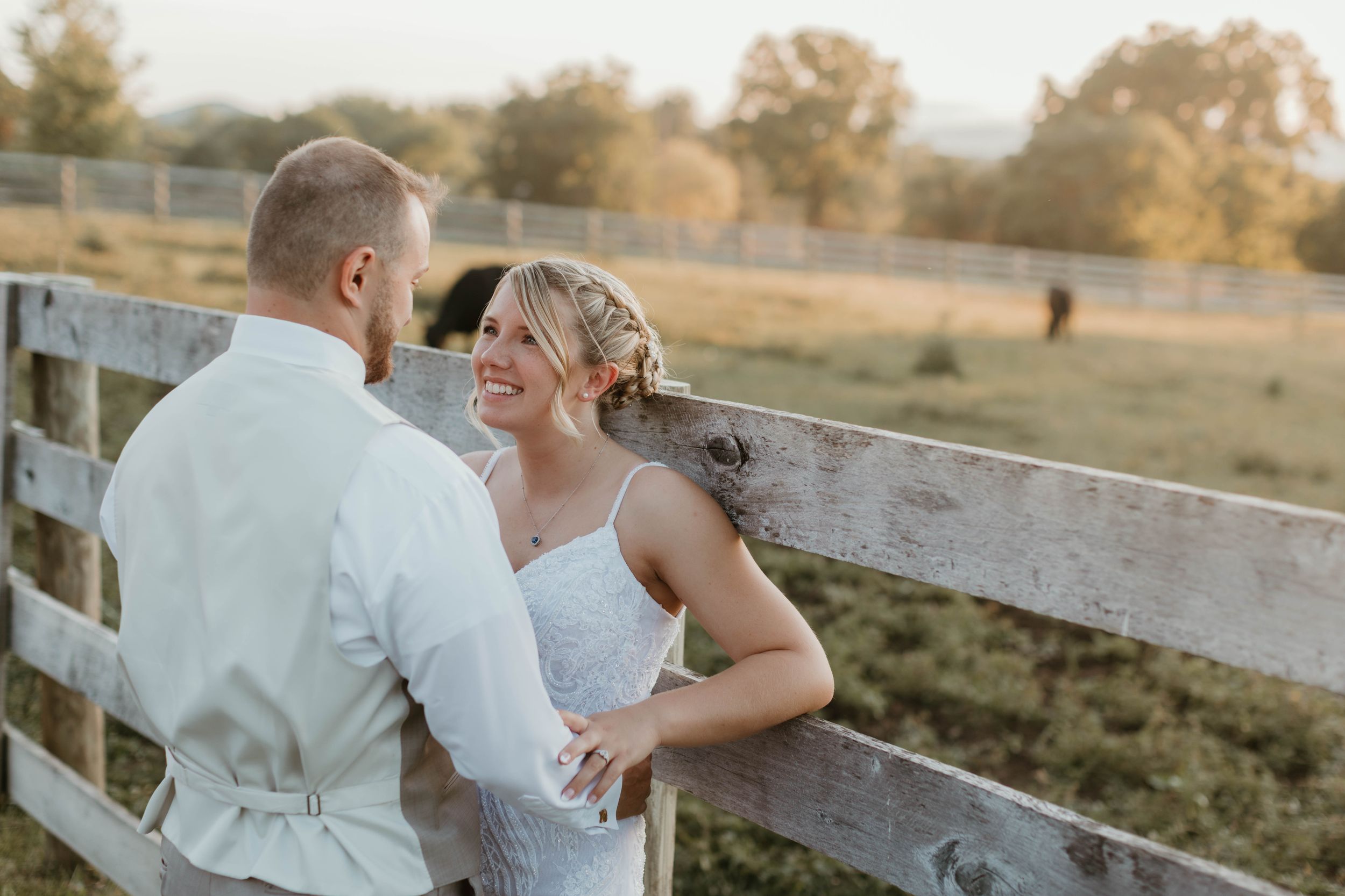 A couple shares a tender moment together on a rustic wooden fence at sunset.