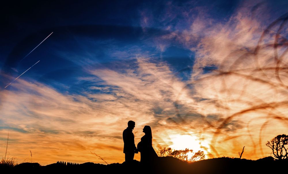 Silhouettes of a couple standing together against a dramatic orange and purple sunset sky.