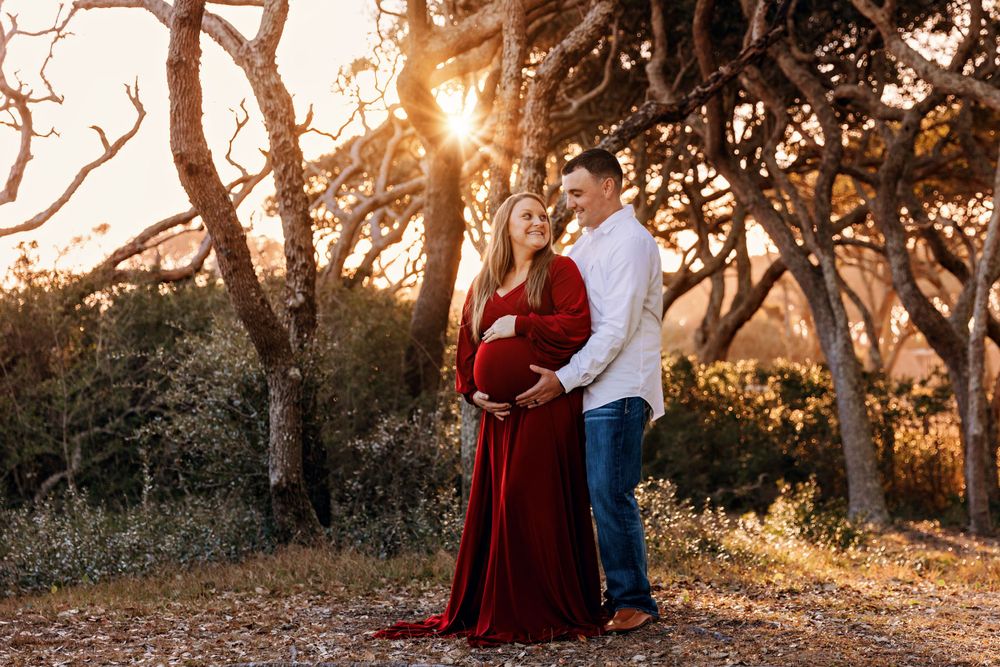 Couple shares intimate moment at sunset among trees during maternity photo session.