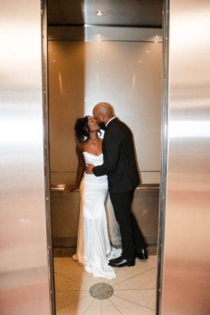 A couple shares a romantic kiss in an elevator during their wedding, with the bride in white and groom in black suit.