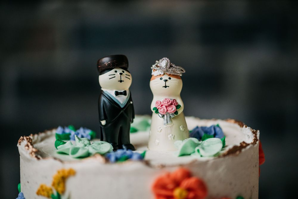 A cute wedding cake topper with bride and groom figurines surrounded by colorful decorative icing on top of a white cake.