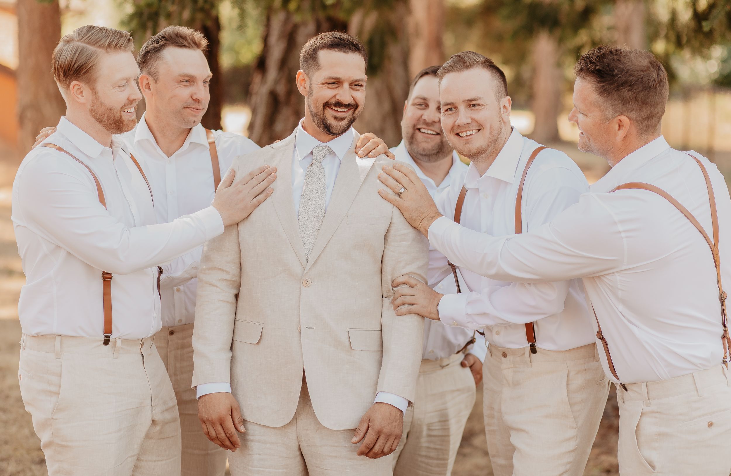 A group wearing matching white outfits laughs and embraces during a joyful outdoor photo session.