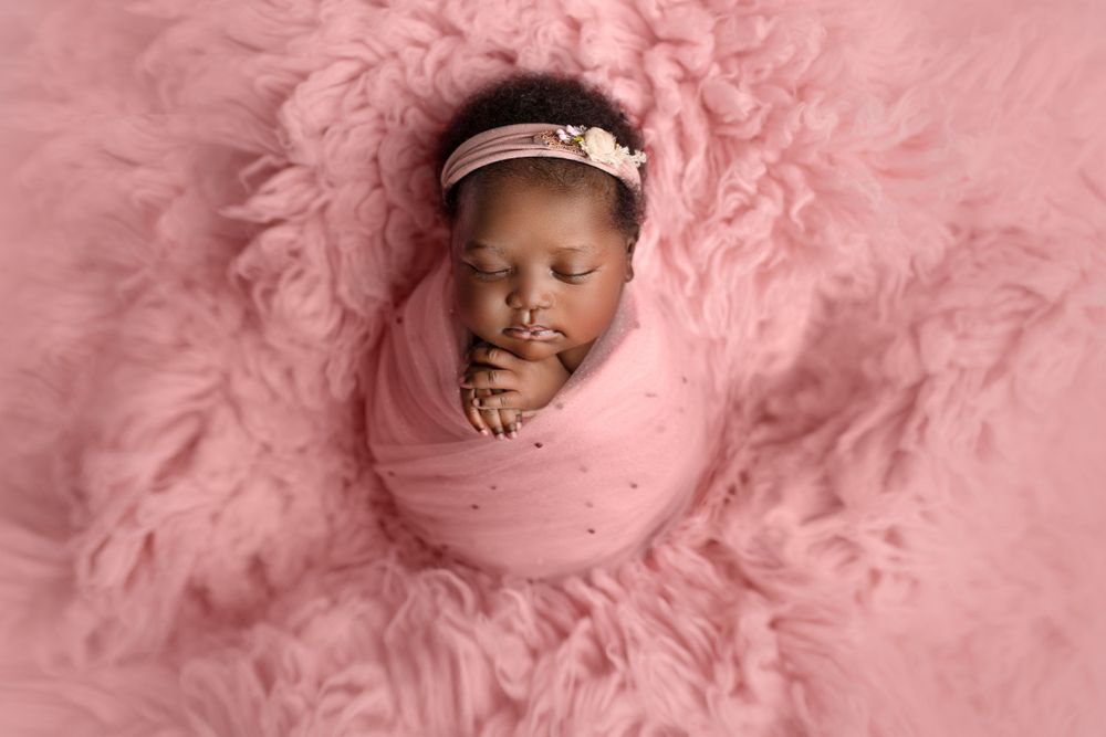 Newborn photography Ipswich and Brisbane – African baby girl wrapped in pink fabric with floral headband, professional studio portraits in S