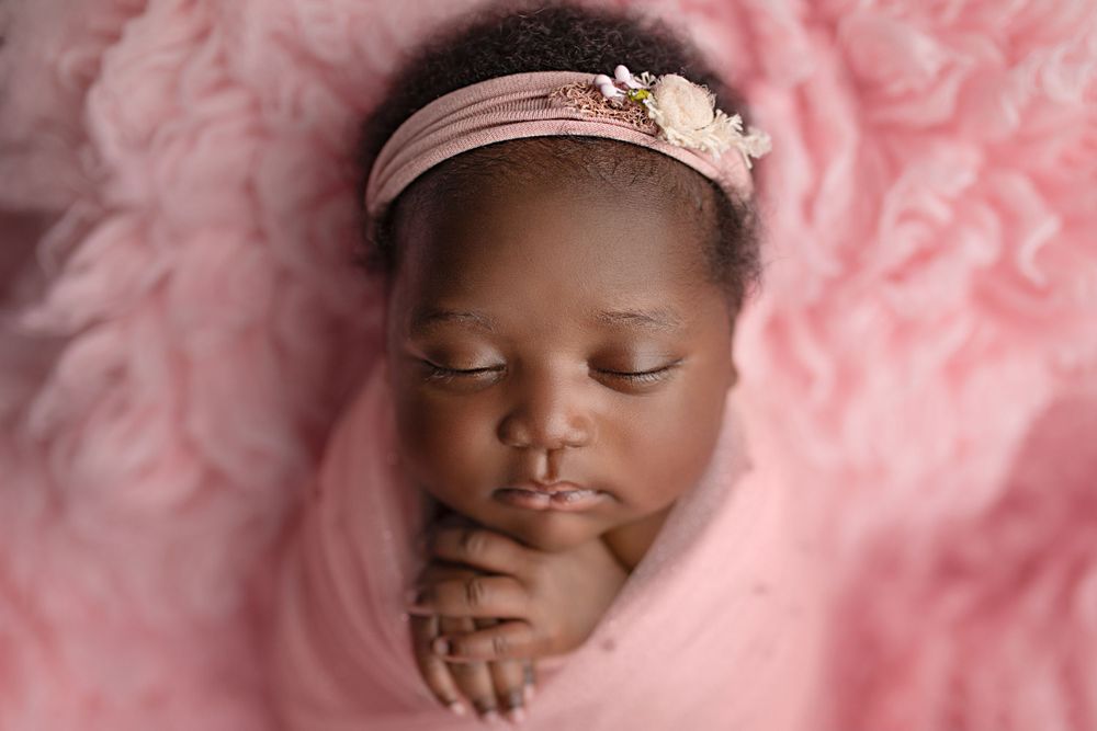 Luxury newborn photographer Springfield Lakes – African baby girl with floral headband resting on pink backdrop, elegant posed portraits for