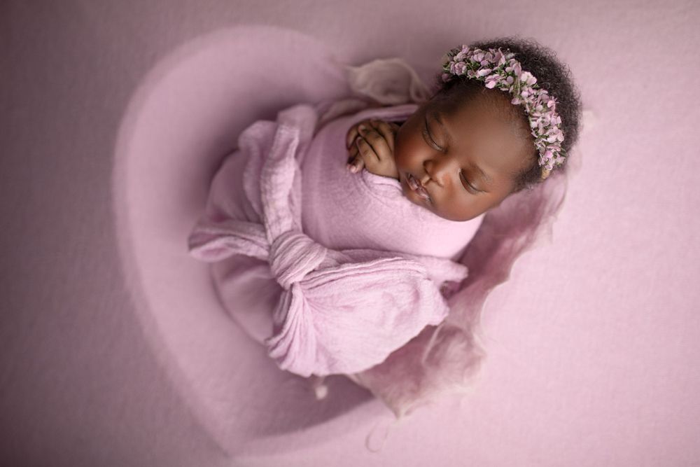 Affordable newborn photography Springfield Lakes – African baby girl with floral crown on heart-shaped pink backdrop, professional portraits
