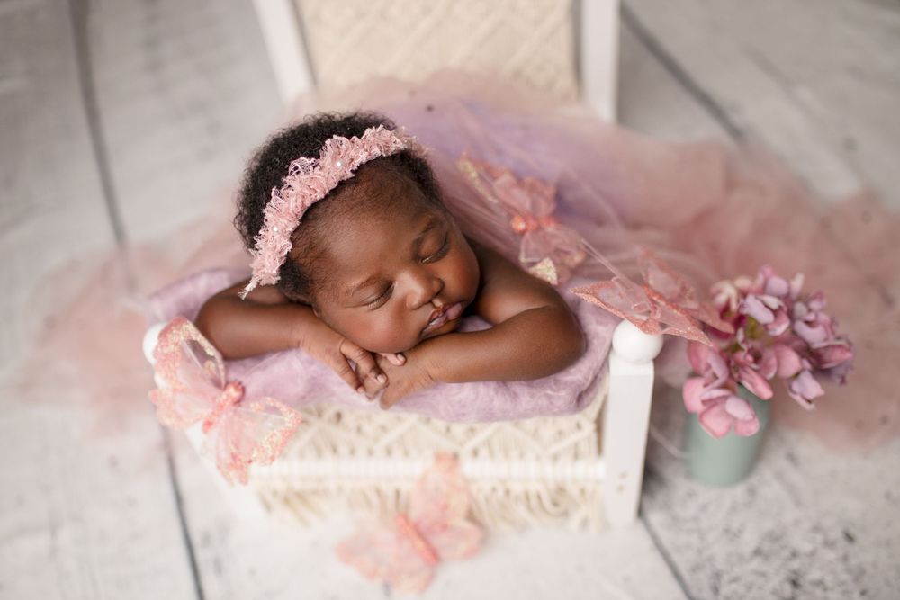 Newborn portraits Springfield Lakes – African baby girl in white wooden basket with pink flowers, professional newborn photography for Ipswi