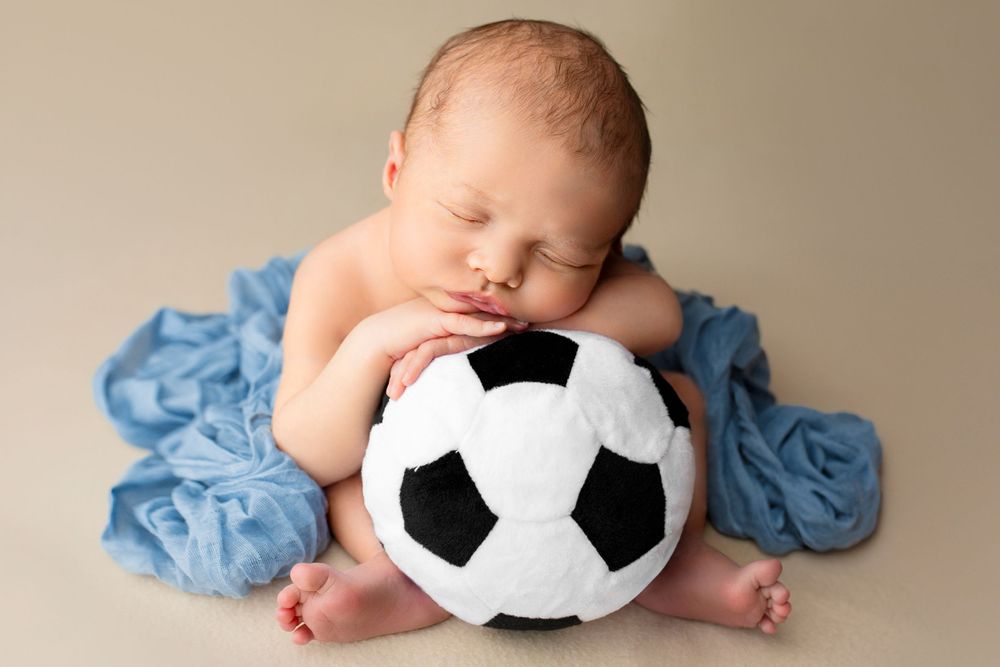 Creative newborn photography Ipswich and Brisbane – baby boy in blue outfit with soccer ball prop, Springfield Lakes studio portraits for Fo