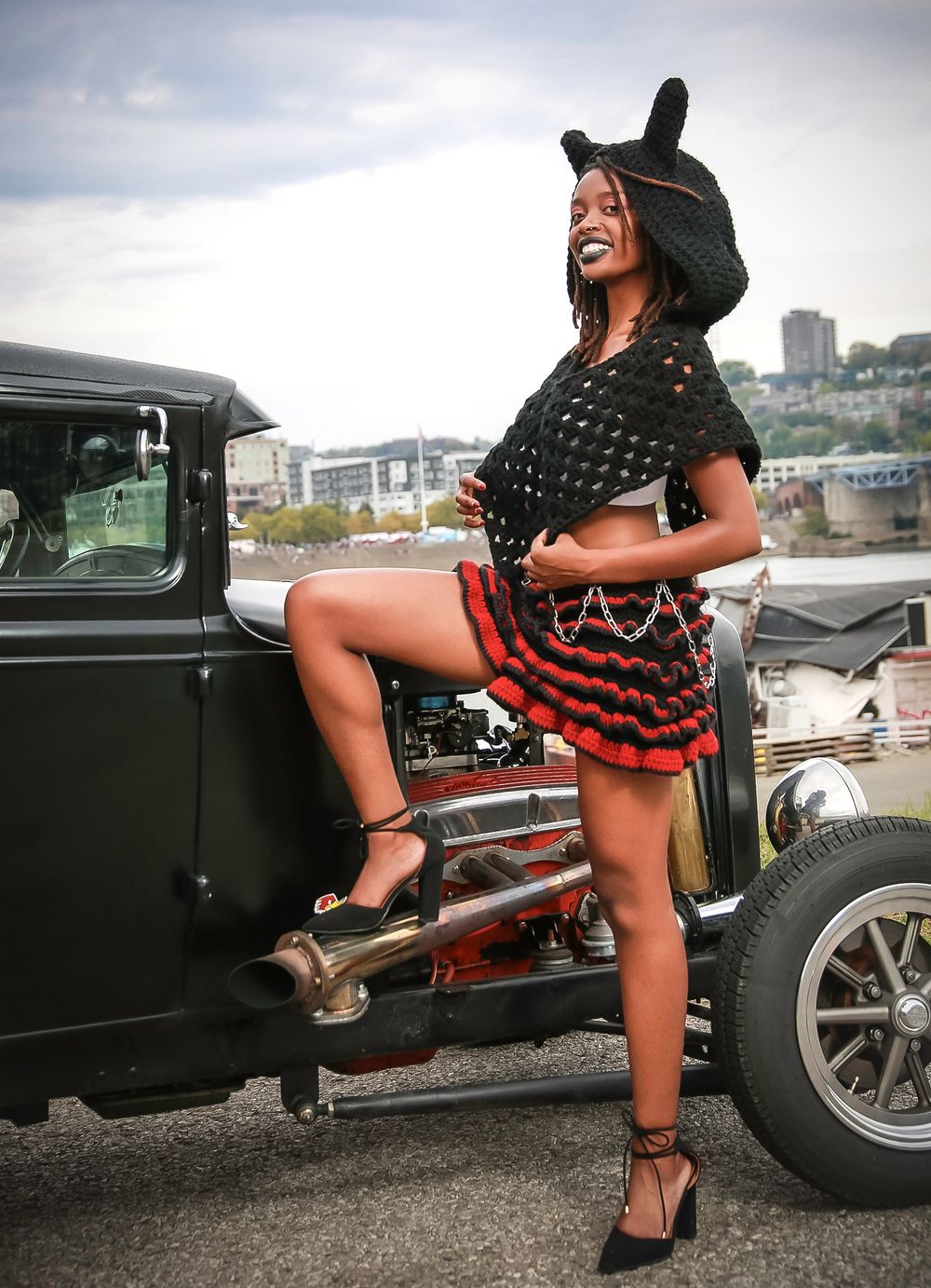A vintage black hot rod parked outdoors while someone poses in a polka dot dress and bunny ear hat against the car.