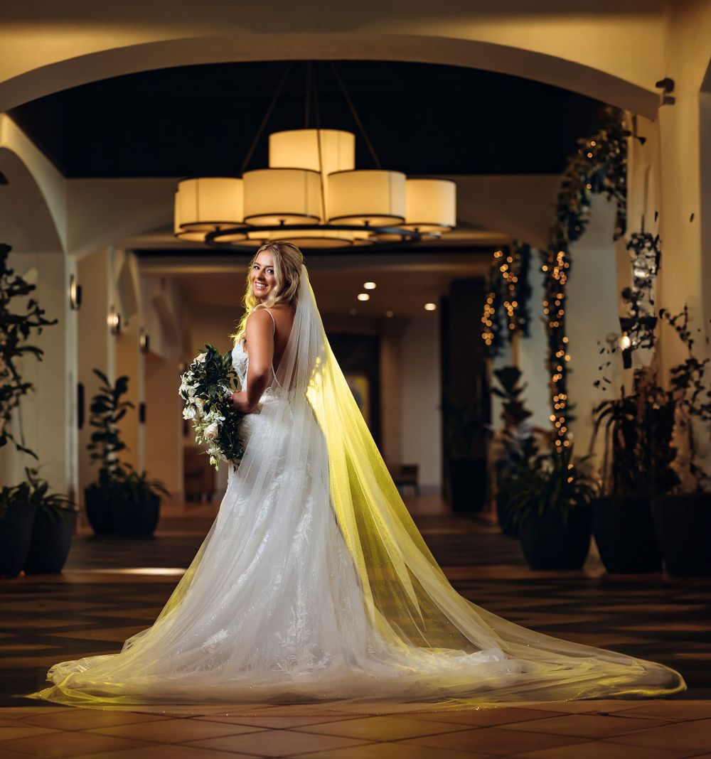 Bride in flowing wedding gown with cathedral veil illuminated by warm lighting.