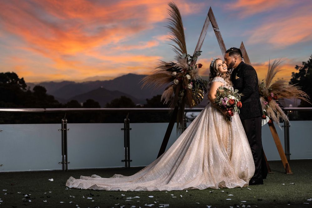 Couple shares romantic moment on balcony against stunning sunset and mountain backdrop.