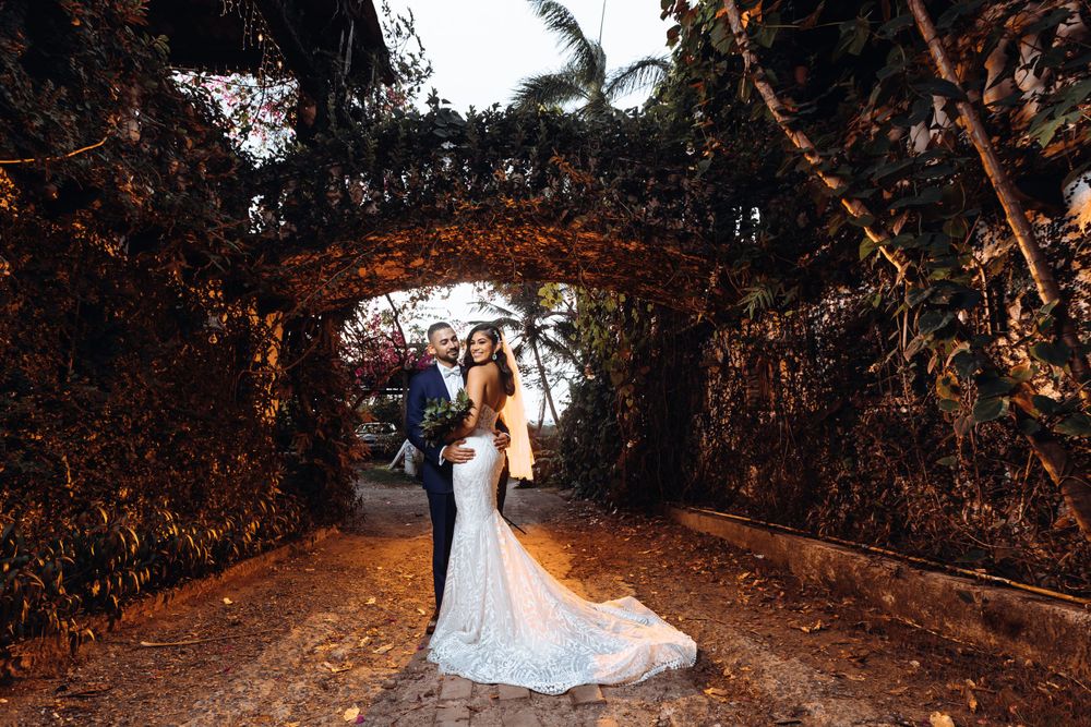 Elegant wedding couple poses beneath a romantic garden archway adorned with climbing vines.