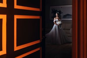 Wedding couple dancing in a dimly lit venue with dramatic orange lighting and silhouetted guests watching.