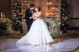 A couple shares an intimate dance in an ornate ballroom decorated with floral arrangements and chandeliers.