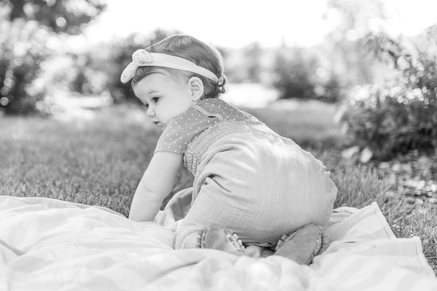 Black and white portrait of baby crawling on blanket outdoors wearing headband.