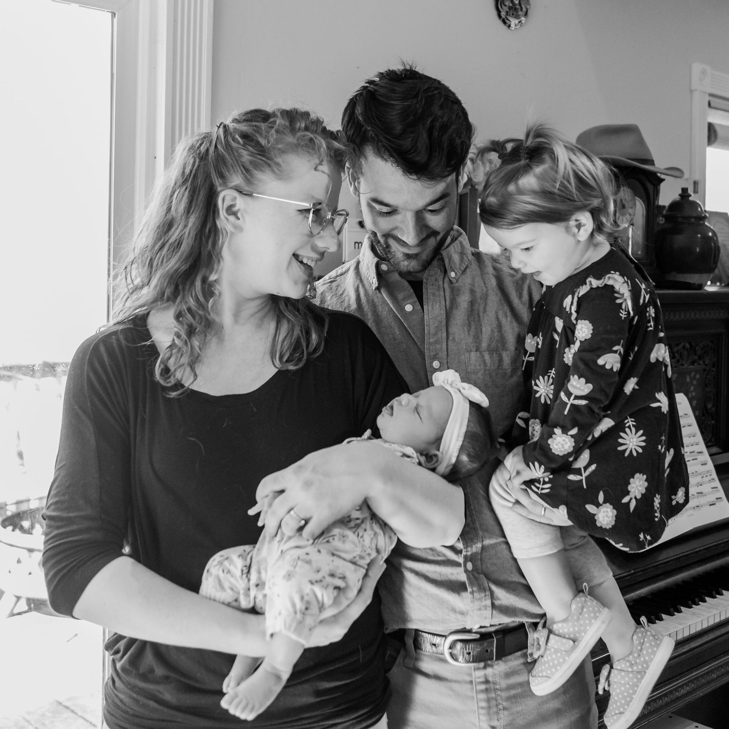 Black and white family moment showing parents with children gathered around piano.
