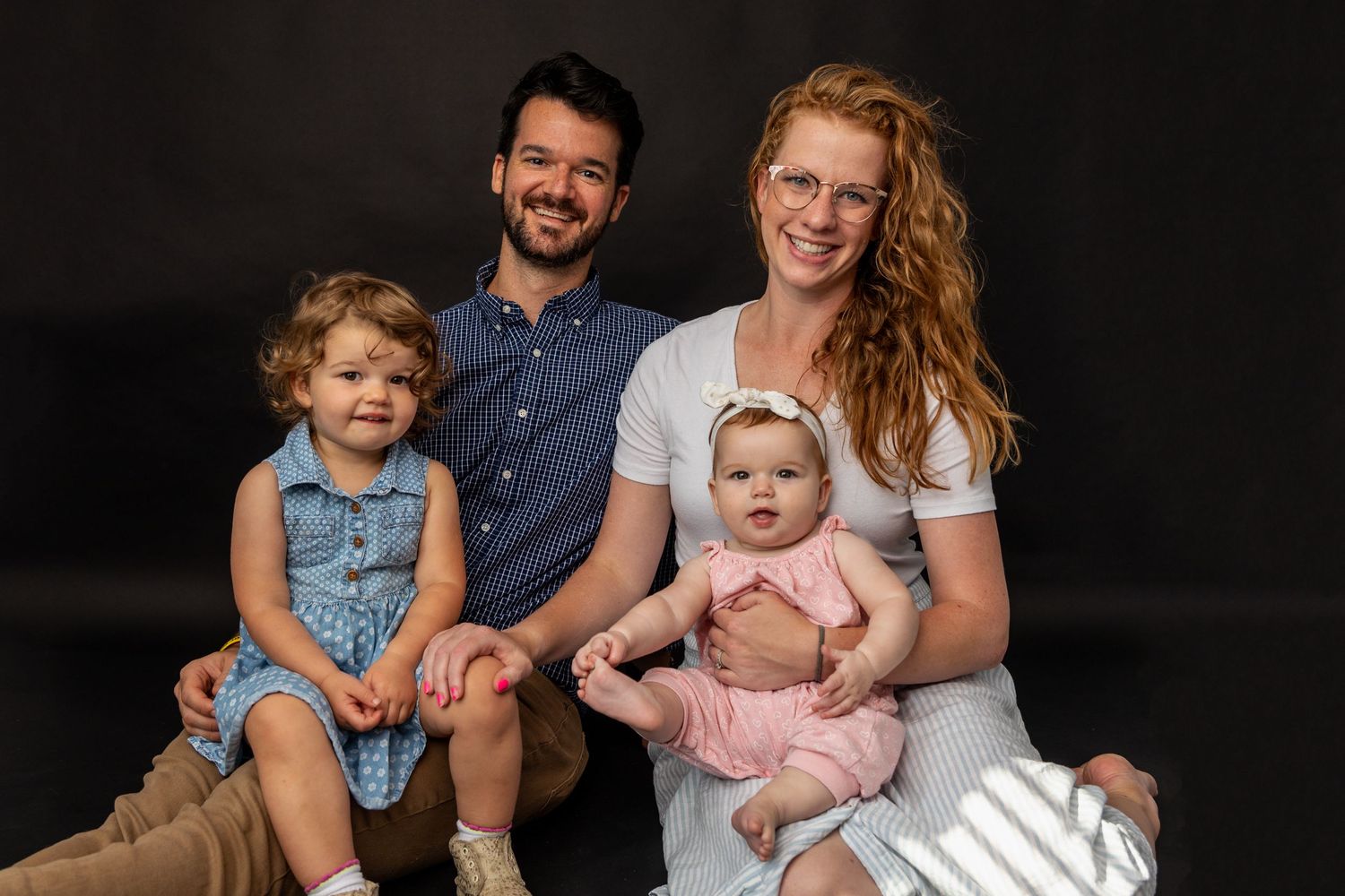 Family portrait session against dark background in studio setting.