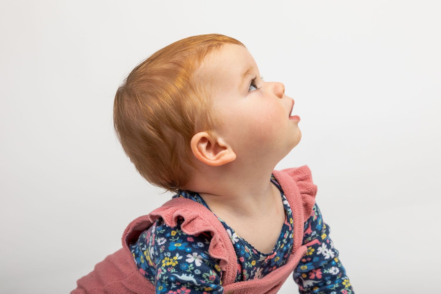 Baby in floral outfit looking up against white background.