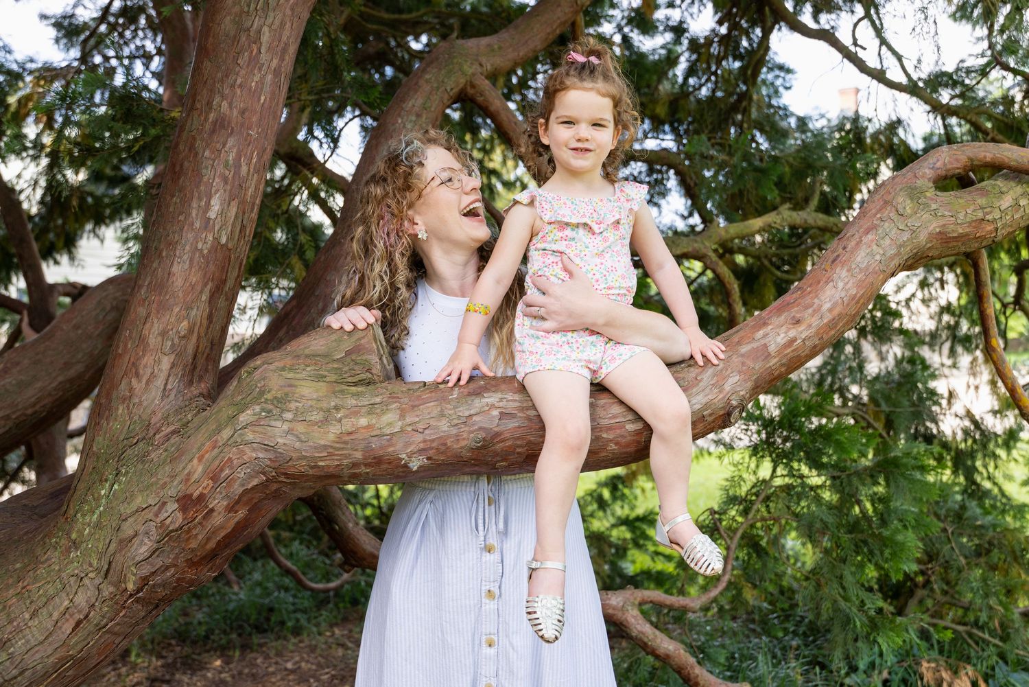 Children playing and climbing on a large tree branch in a sunny outdoor setting.