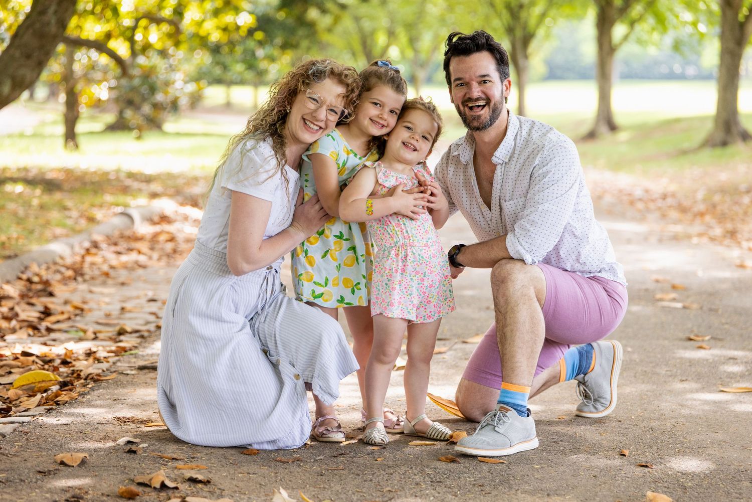 Family of four posing together on autumn path with fallen leaves.