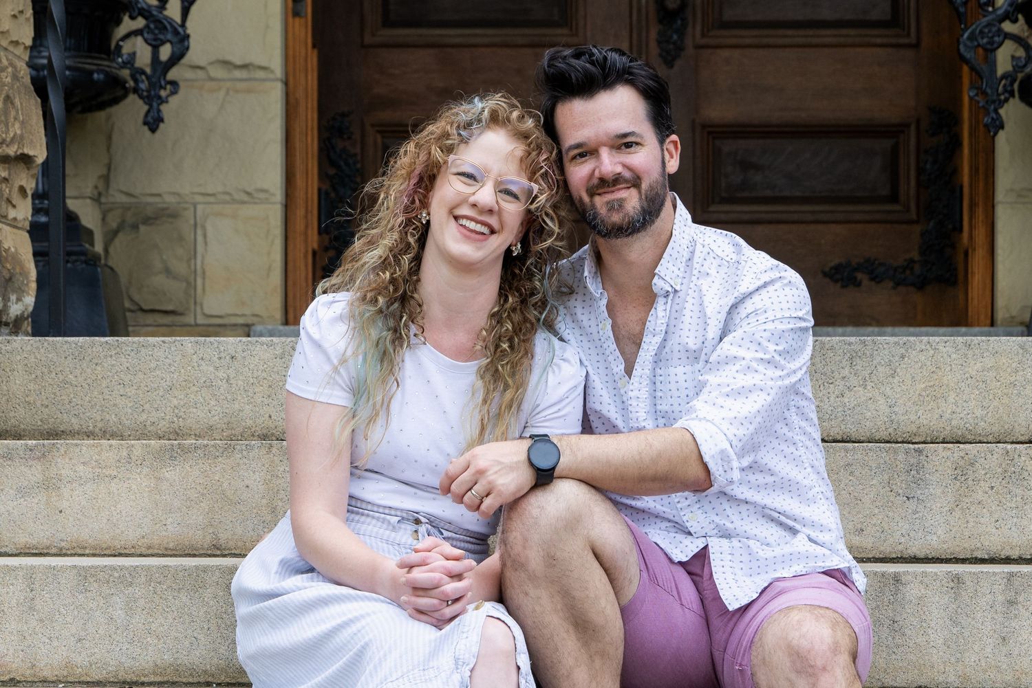 Couple sitting together on stone steps outside a building entrance.