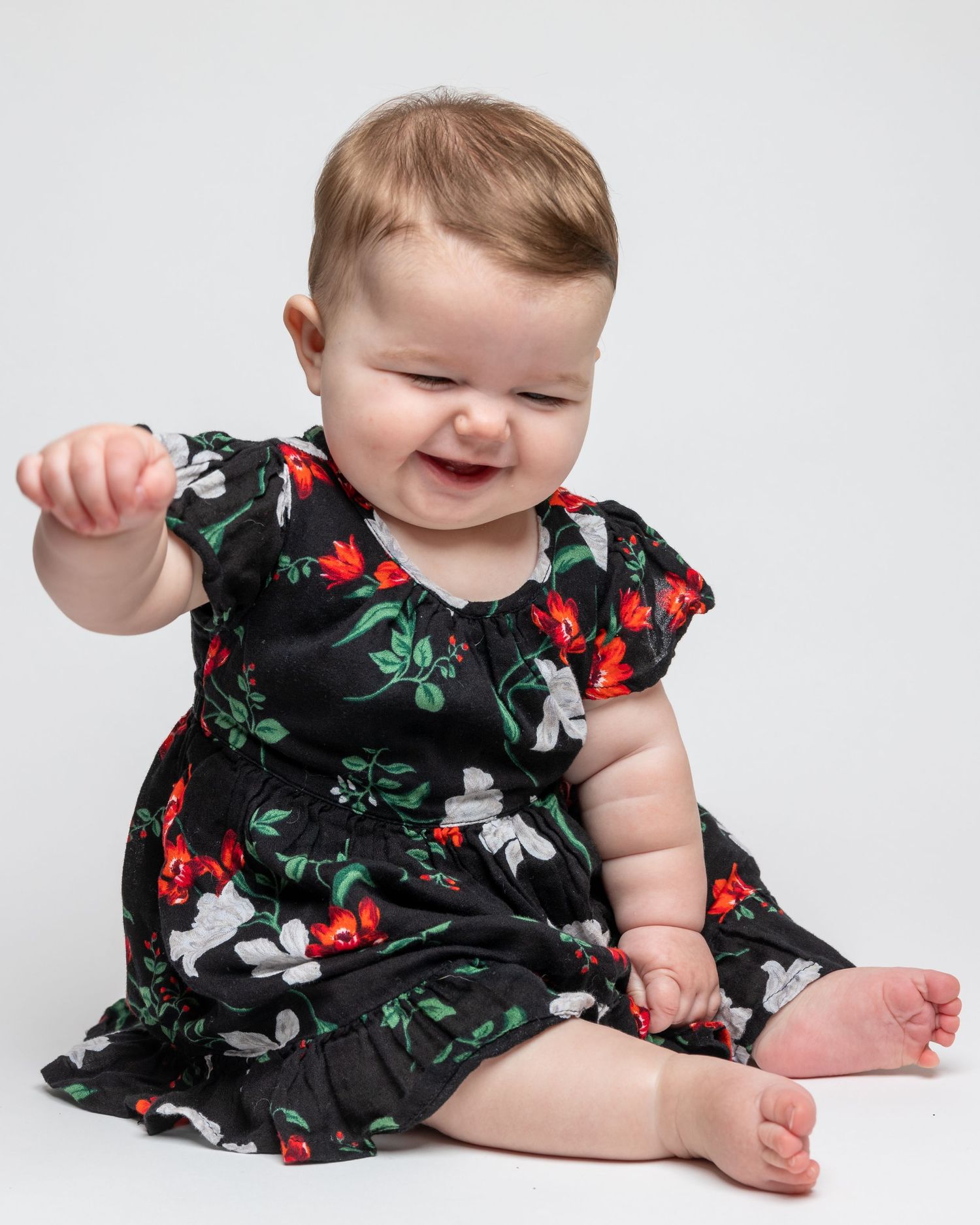 Baby wearing floral dress lying on white background during studio photoshoot.