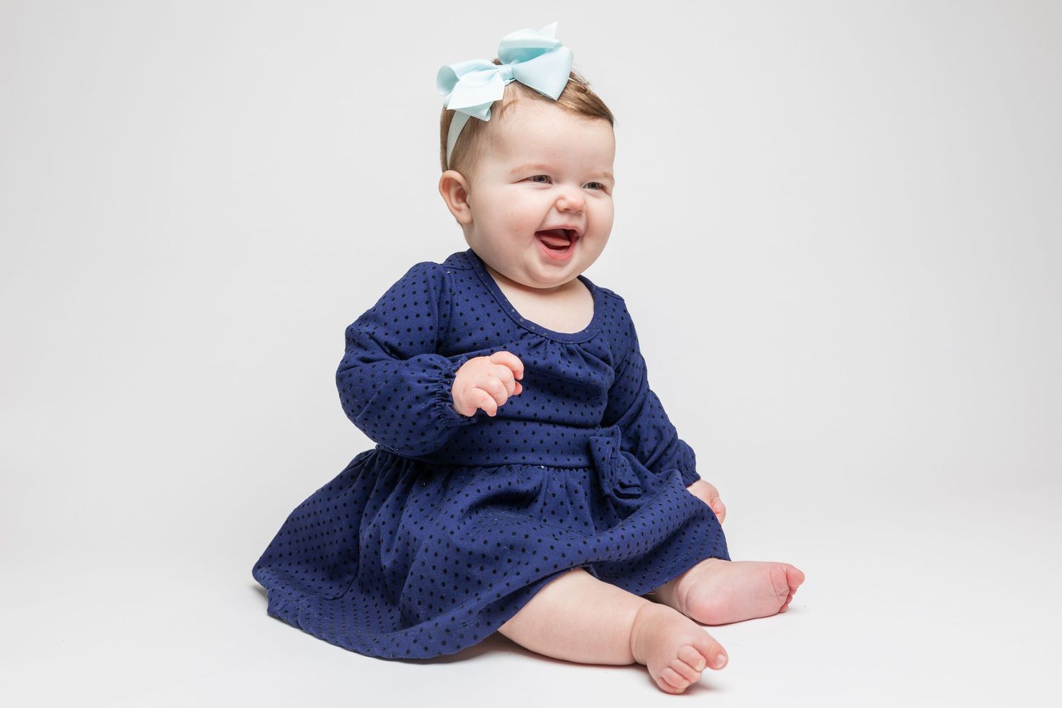 Baby in navy blue dress posing on white studio background.