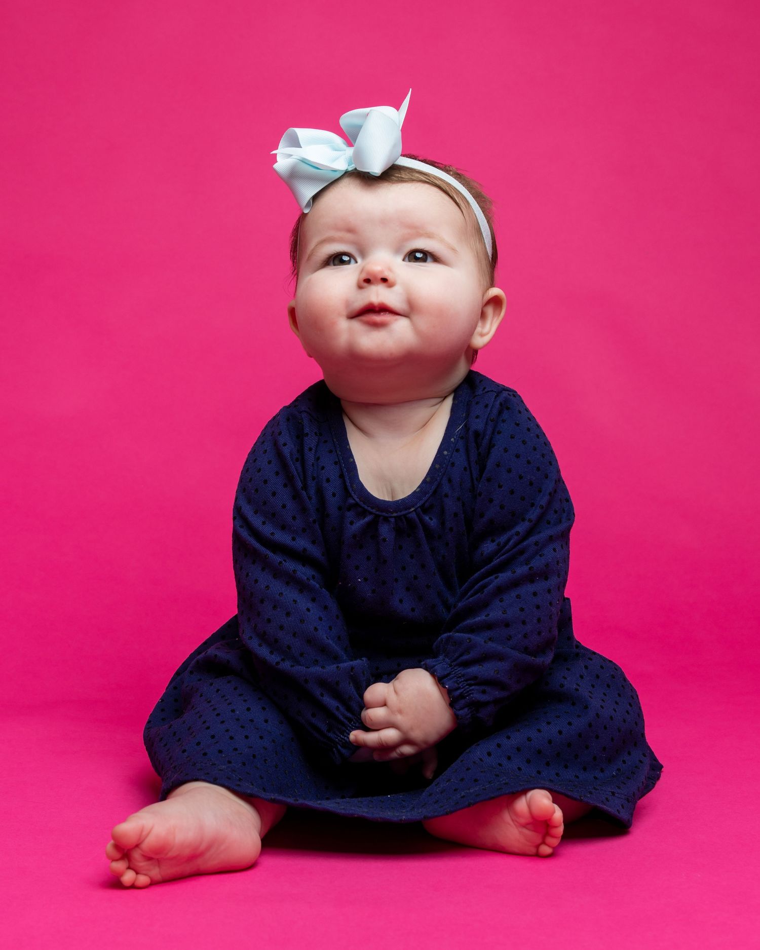 Baby in navy dress photographed against bright pink studio backdrop.