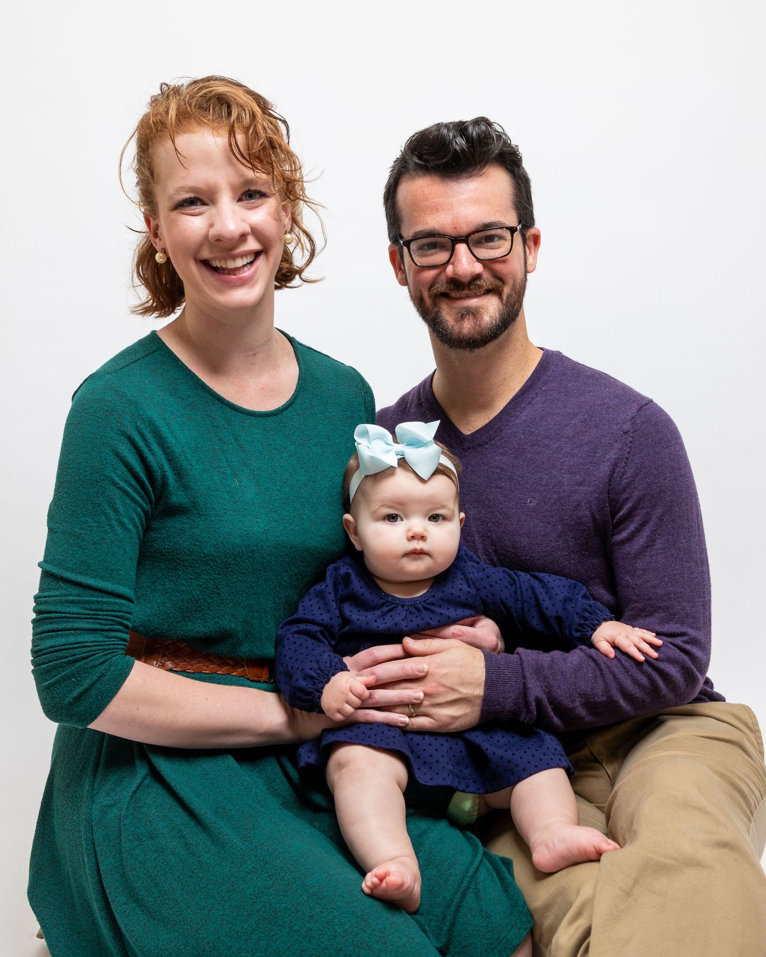 Family portrait session with parents and baby against white studio background.