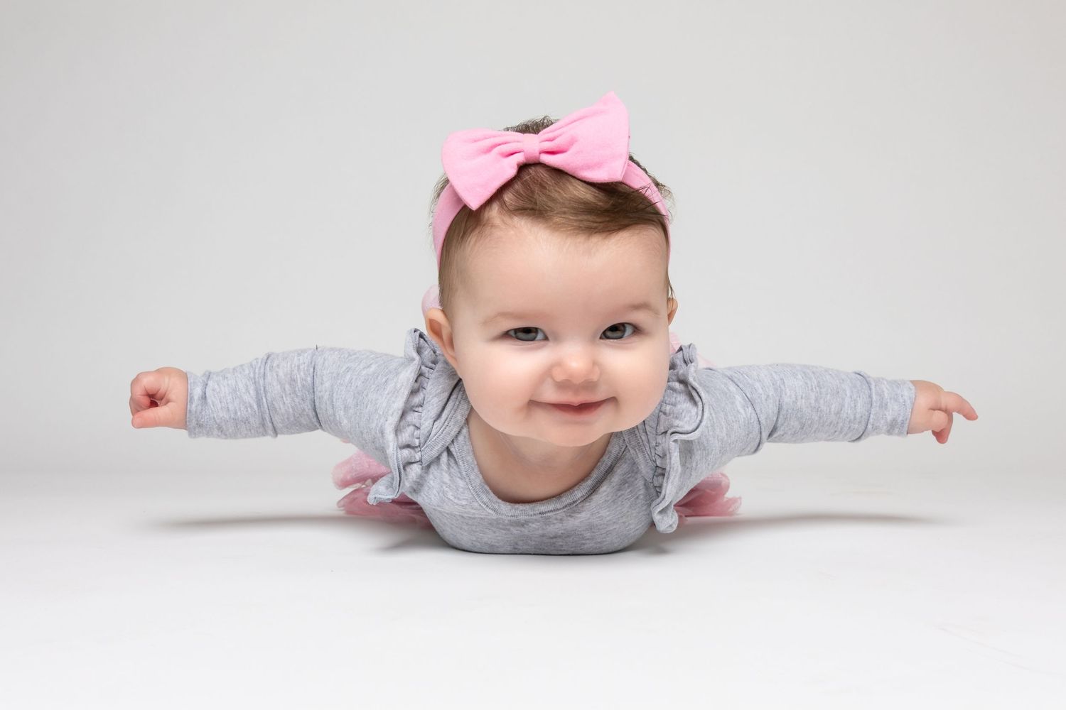 Baby wearing pink bow crawling on white studio floor during photoshoot.