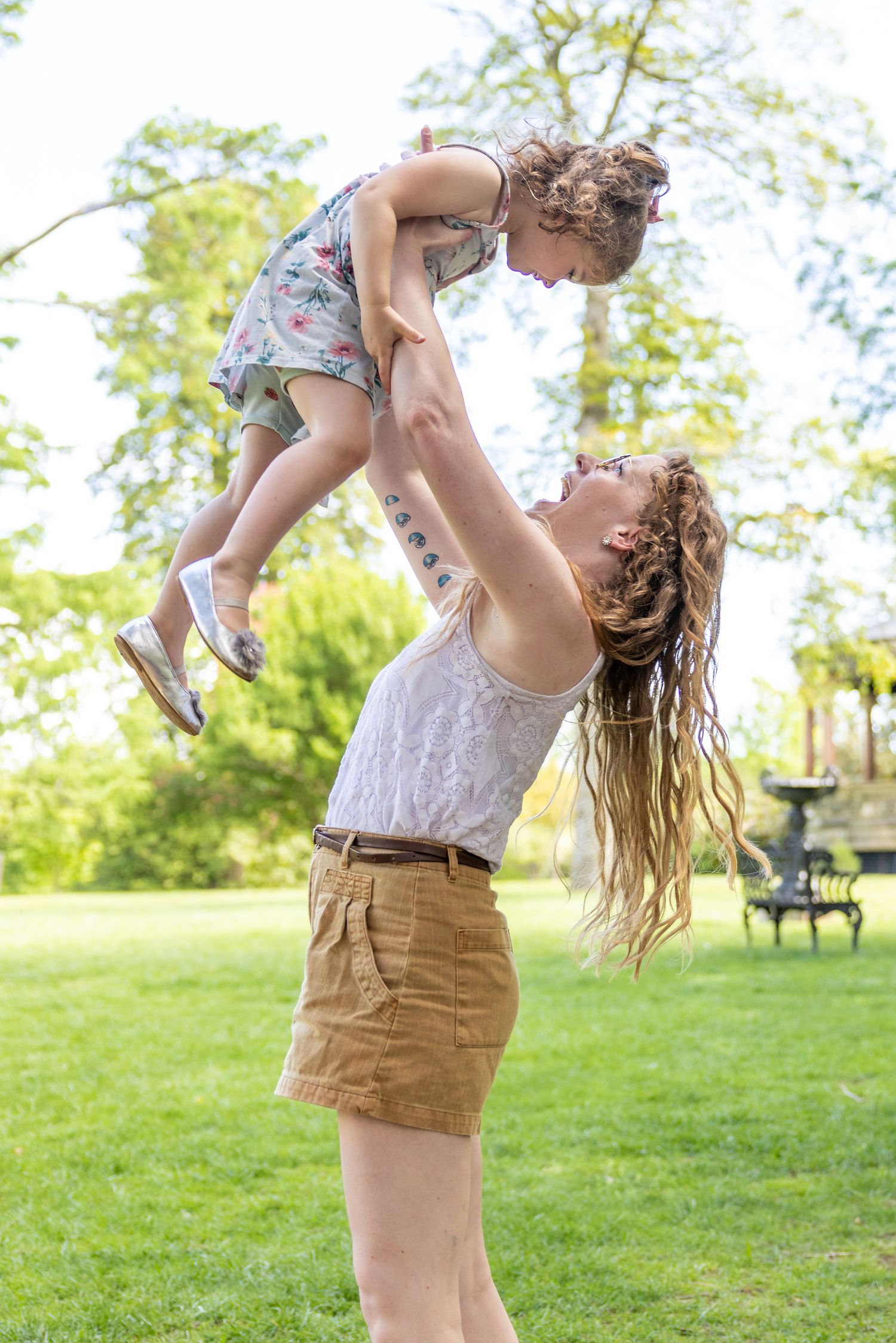 Joyful outdoor moment with parent lifting child in the air at park.