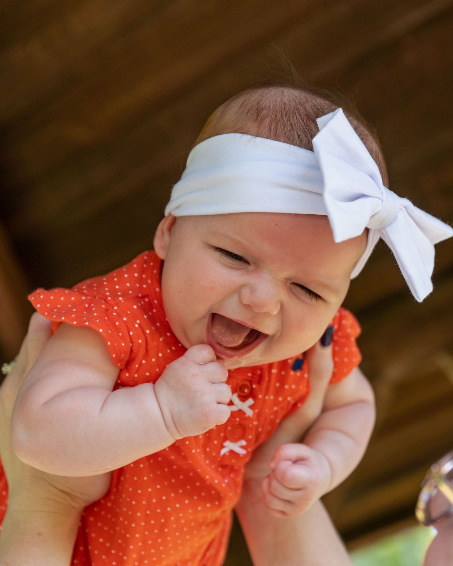 Happy baby wearing coral polka dot dress and white bow headband.