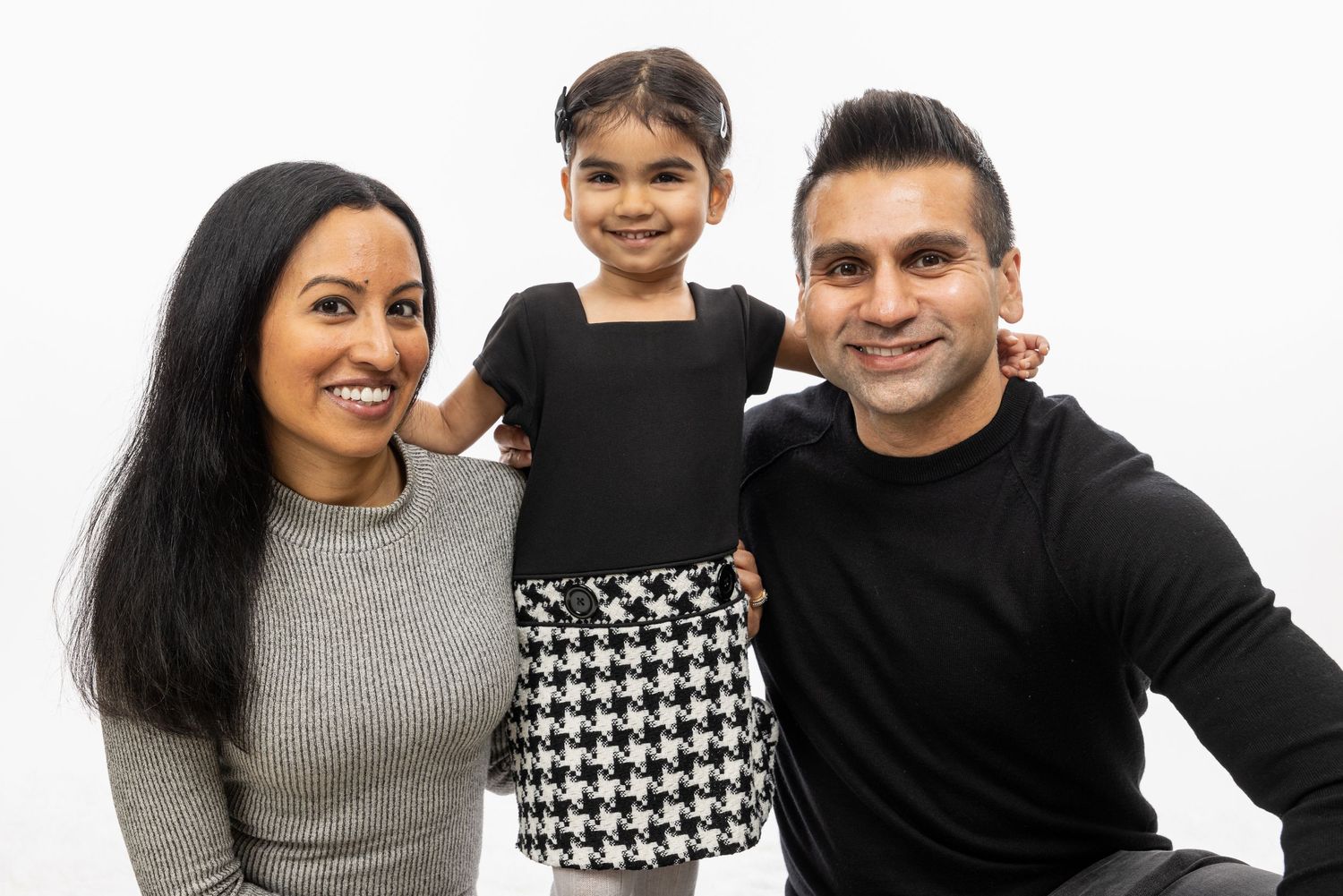 Family portrait against white background showing parents and young child in coordinated outfits.