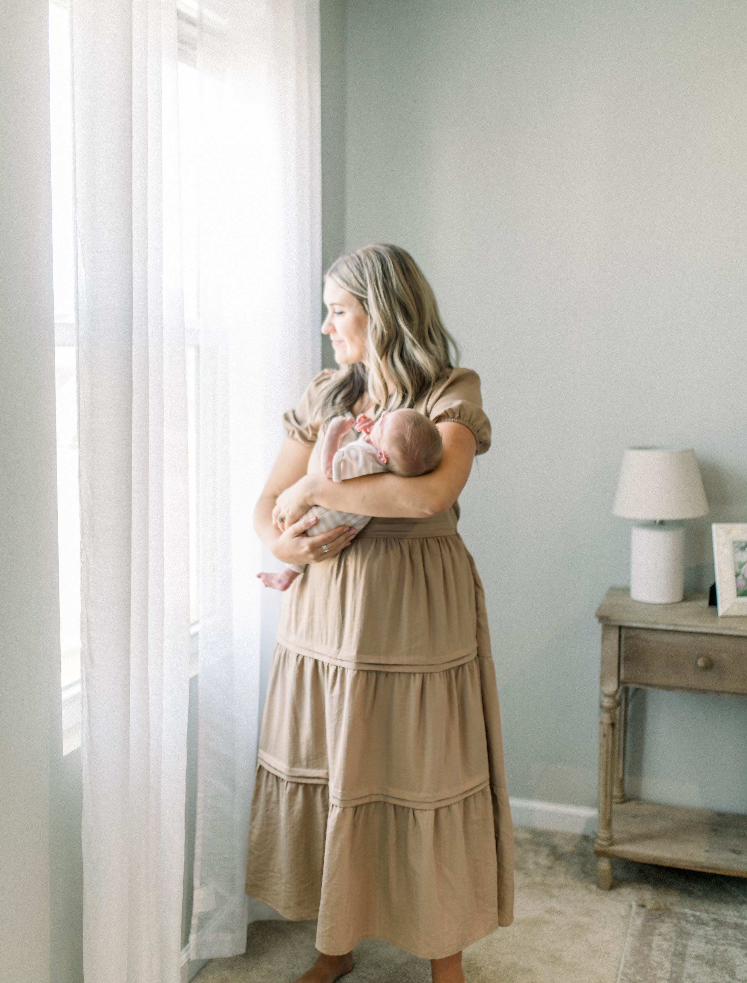 A simple and elegant photo of mother and newborn looking out window at their home captured by photographer in Greenville, South Carolina