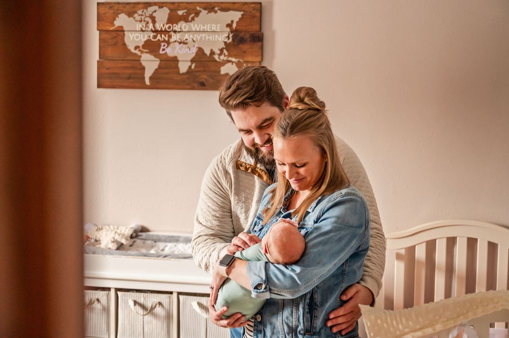 A person in a blue shirt sits in a nursery room with a world map on the wall while holding a baby.