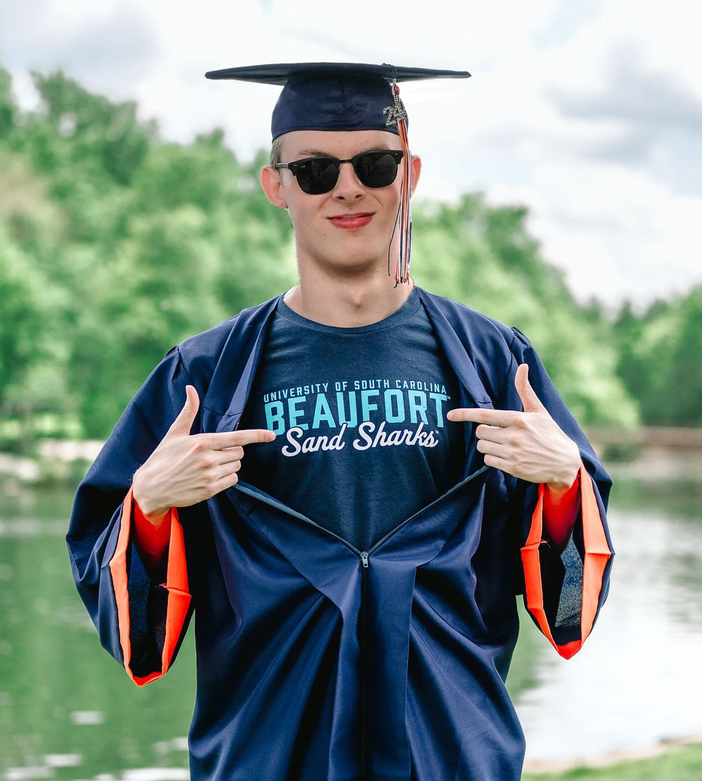 Graduate in sunglasses and blue gown showing off Beaufort School Sciences text.
