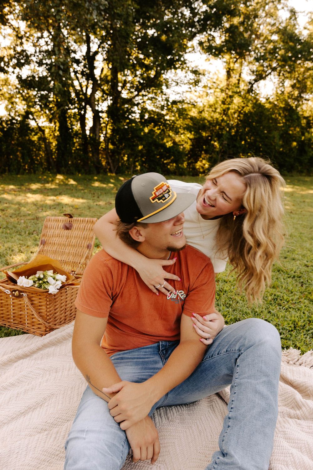 Couple enjoying romantic picnic on blanket at sunset with wicker basket in grassy park setting.