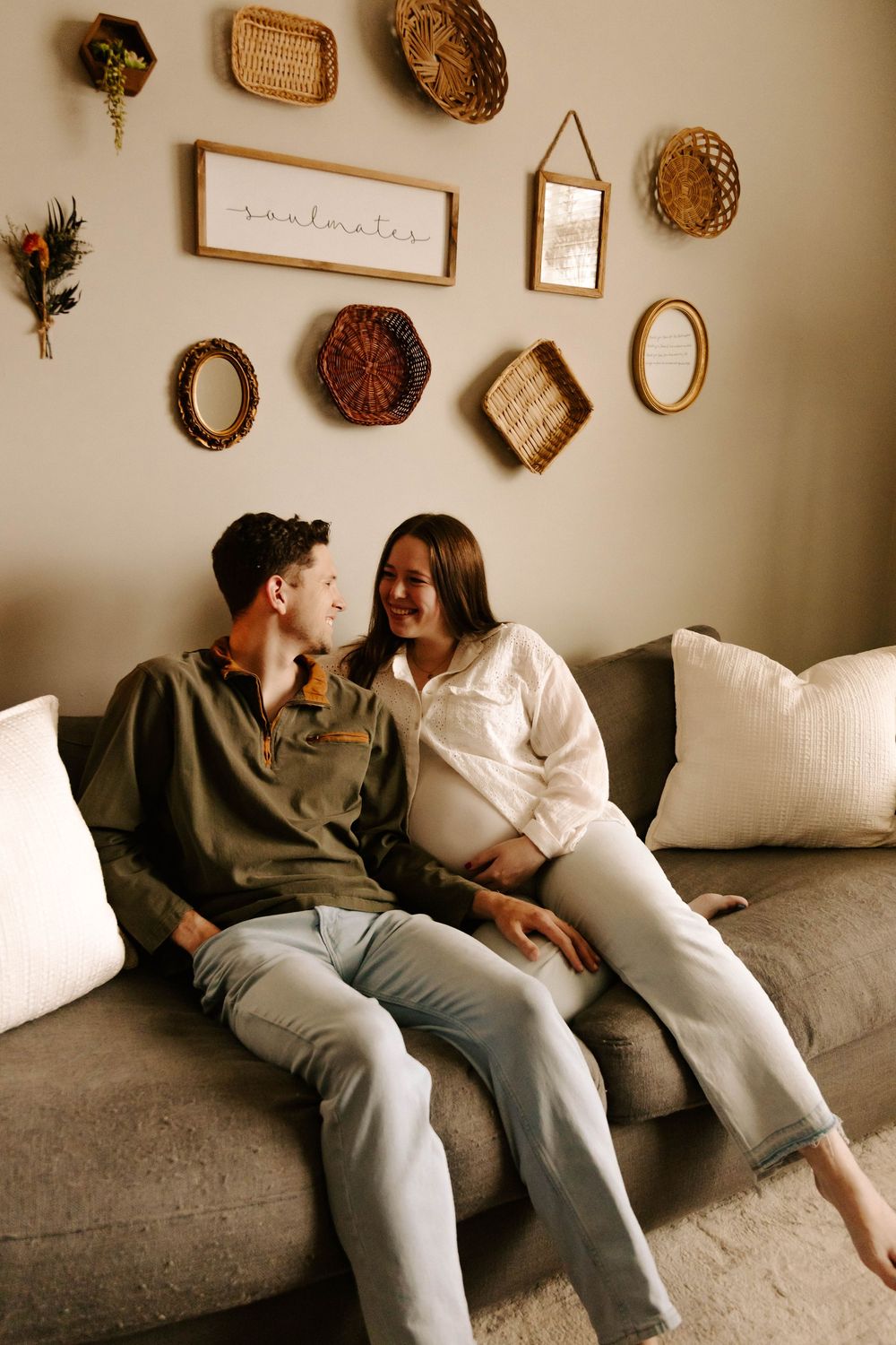 A couple shares an intimate moment on a grey couch beneath a gallery wall of decorative vintage frames and wall art.