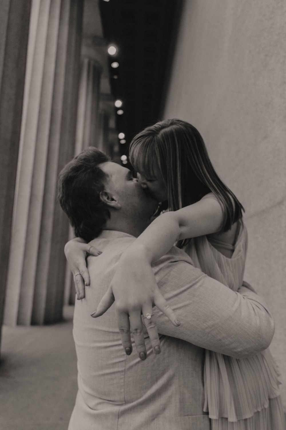 Romantic black and white photograph of a couple sharing an intimate embrace and kiss outdoors at night.