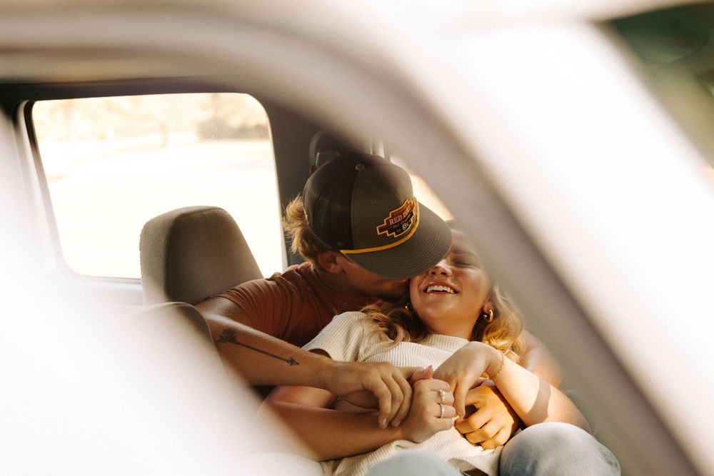 A couple shares a tender moment while sitting in a car on a sunny day.