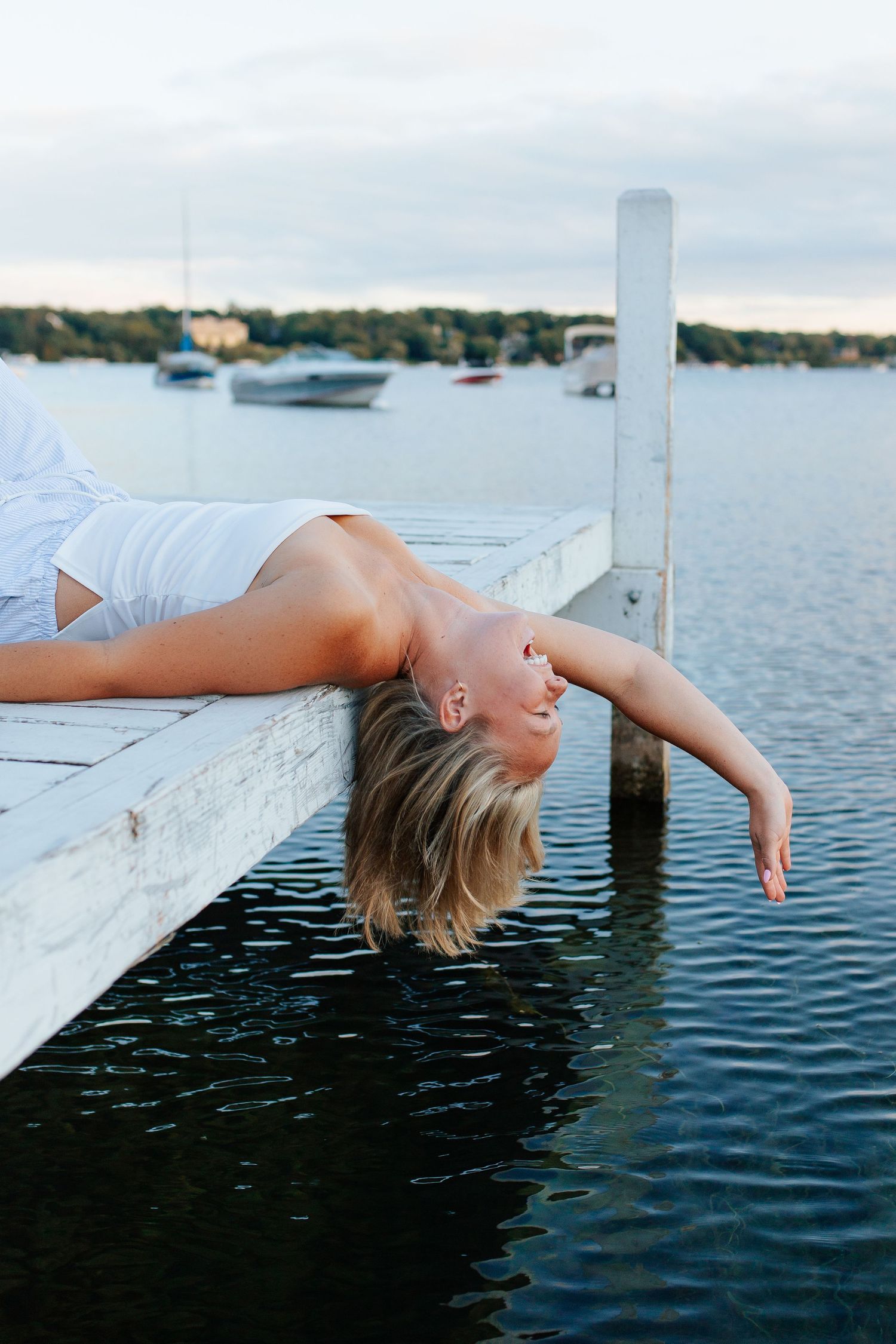 Person lying on dock above tranquil water during golden hour. Senior photo session. Lake Geneva Wisconsin Photographer