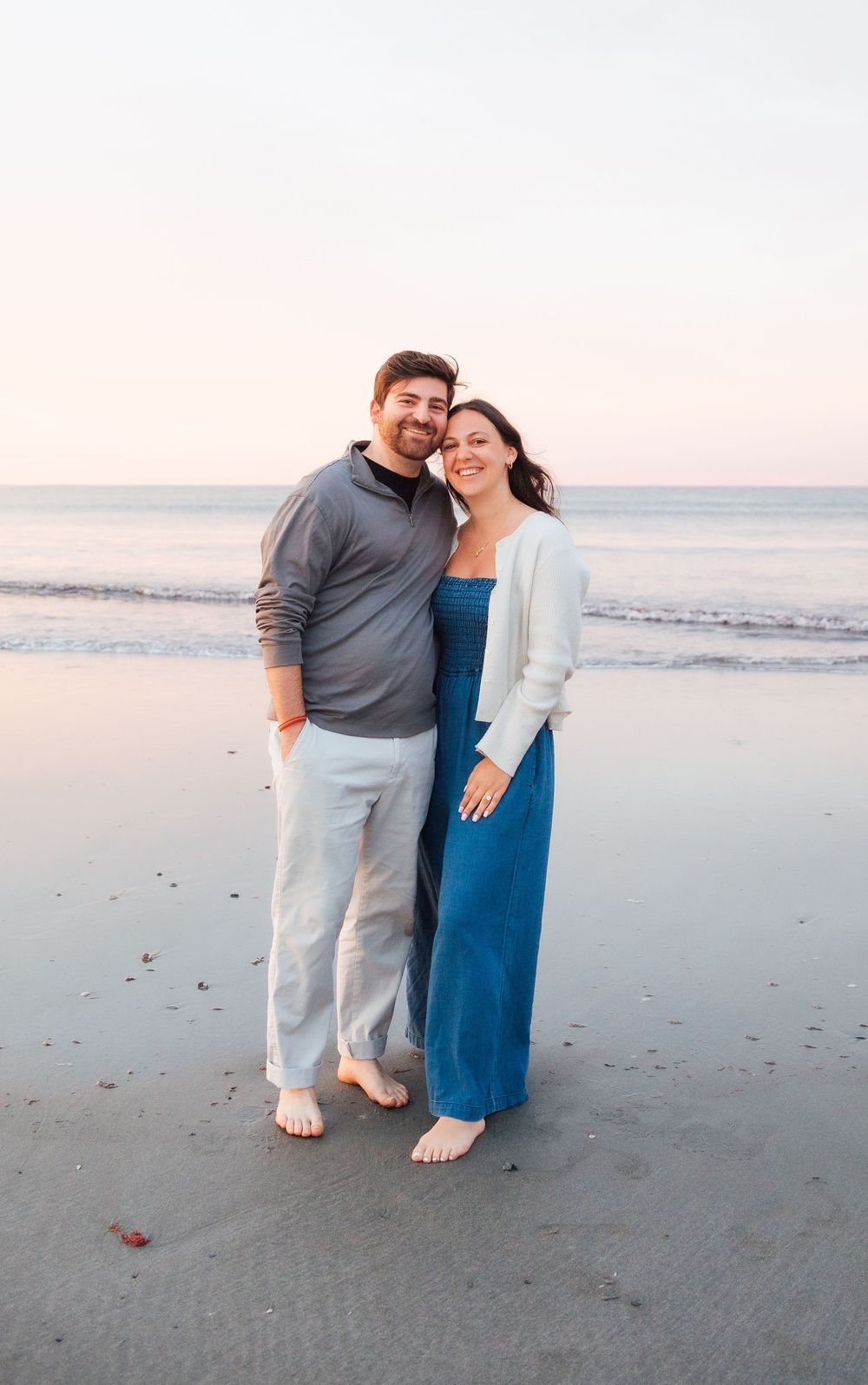 Couple smiling together on a sandy beach at sunset, woman in blue dress and man in gray sweater. Second Beach Middletown Rhode Island