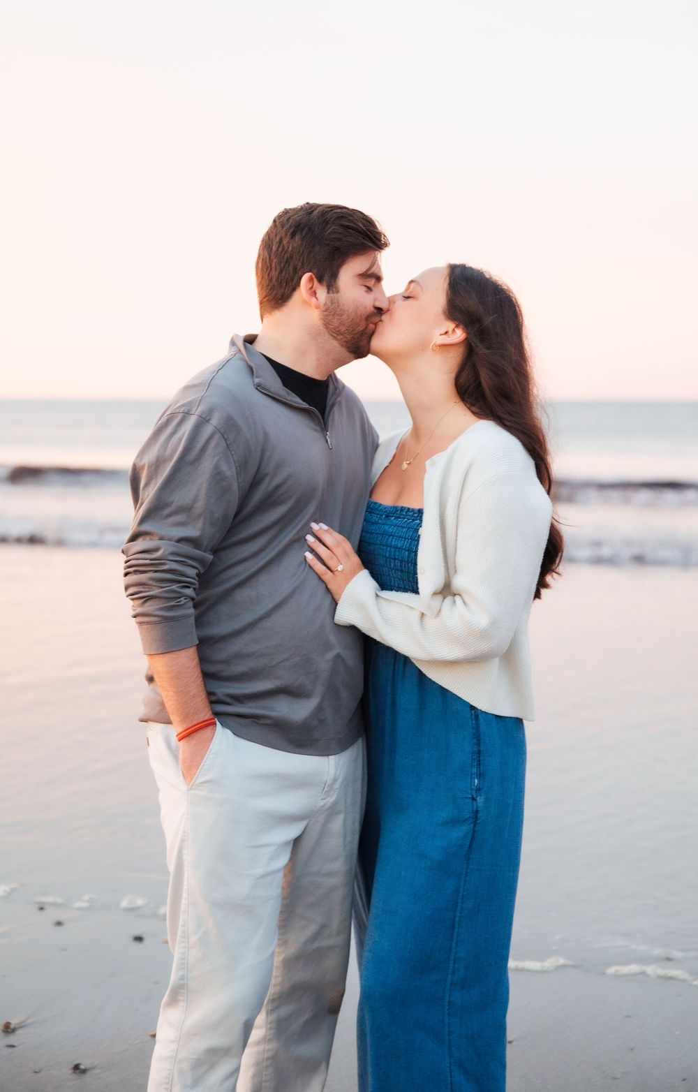 A couple shares a romantic kiss on the beach at sunset, the woman in a blue dress and white cardigan. Second Beach Middletown Rhode Island