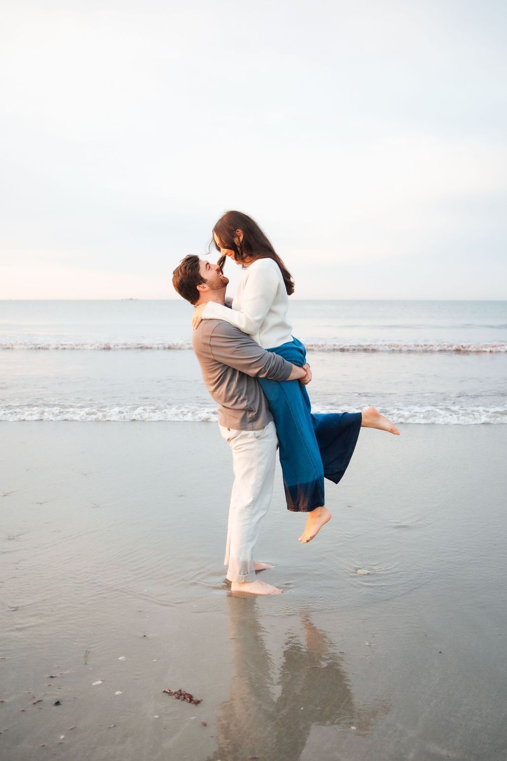 A couple shares a romantic kiss on the beach, as the man lifts the woman in his arms near the ocean. Second Beach Middletown Rhode Island