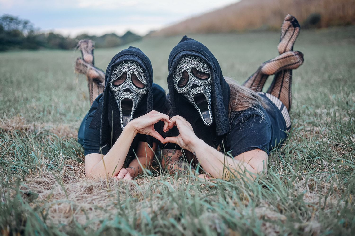 Two people wearing Scream masks making heart shape while lying in grass. Customer photography